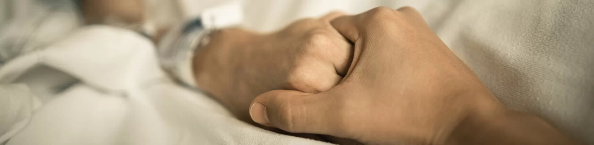 Eine erkrankte Person hält vertrauensvoll die Hände einer Hospiz-Kraft.