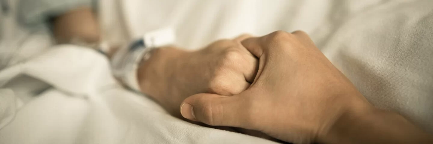 Eine erkrankte Person hält vertrauensvoll die Hände einer Hospiz-Kraft.