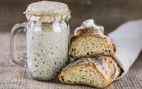 Links steht ein Glas gefüllt mit Sauerteig, rechts ein Sauerteigbrot.