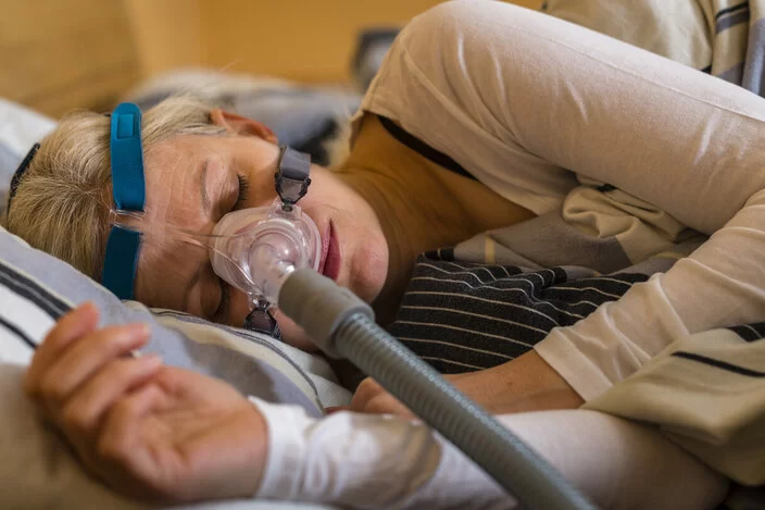 Eine Frau schläft auf einem Bett und benutzt eine CPAP-Maschine.