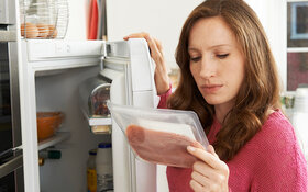 Eine Frau steht vor dem Kühlschrank und betrachtet verpackte Lebensmittel, um sicherzugehen, dass sie noch nicht verdorben sind.