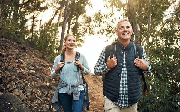 Ein Mann und eine Frau wandern mit Rucksäcken gut gelaunt an einem Waldhang.