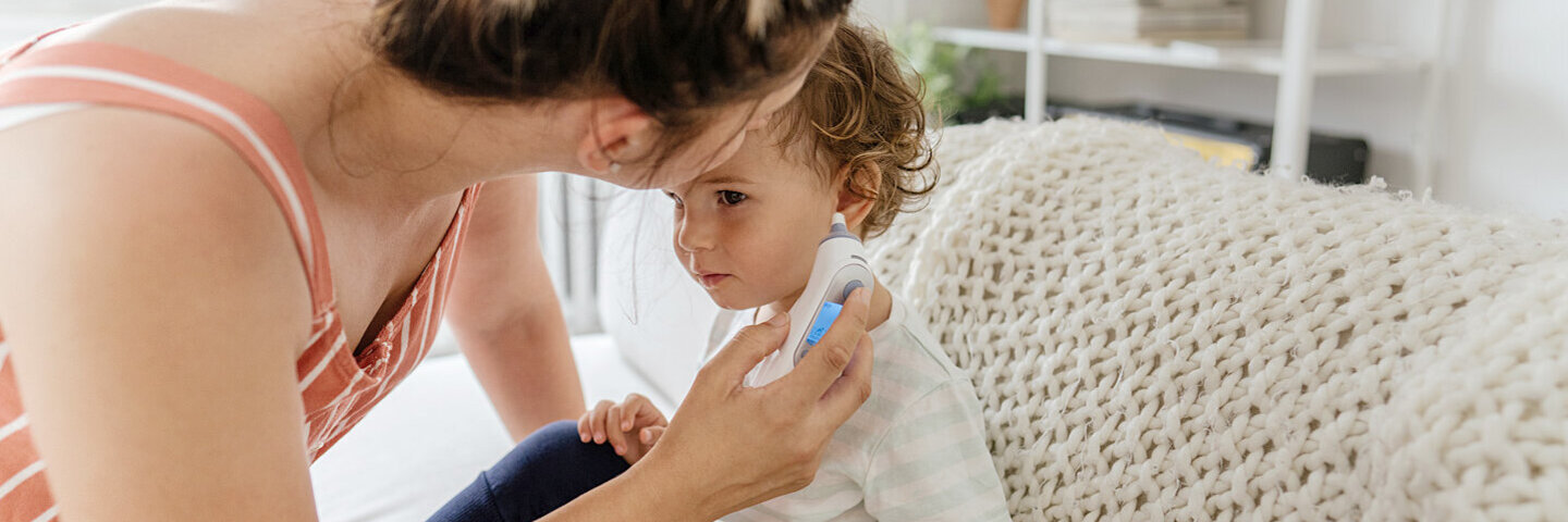 Eine Frau misst bei ihrem Kind Fieber im Ohr.