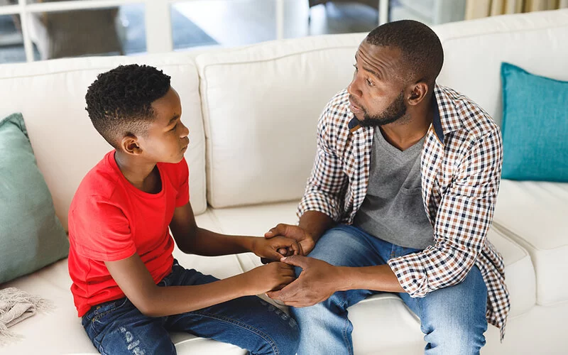 Vater und Sohn sitzen gemeinsam auf dem Sofa und sprechen über toxische Männlichkeit.
