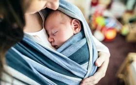 Mutter trägt ihr Baby in einem Tuch vor der Brust.