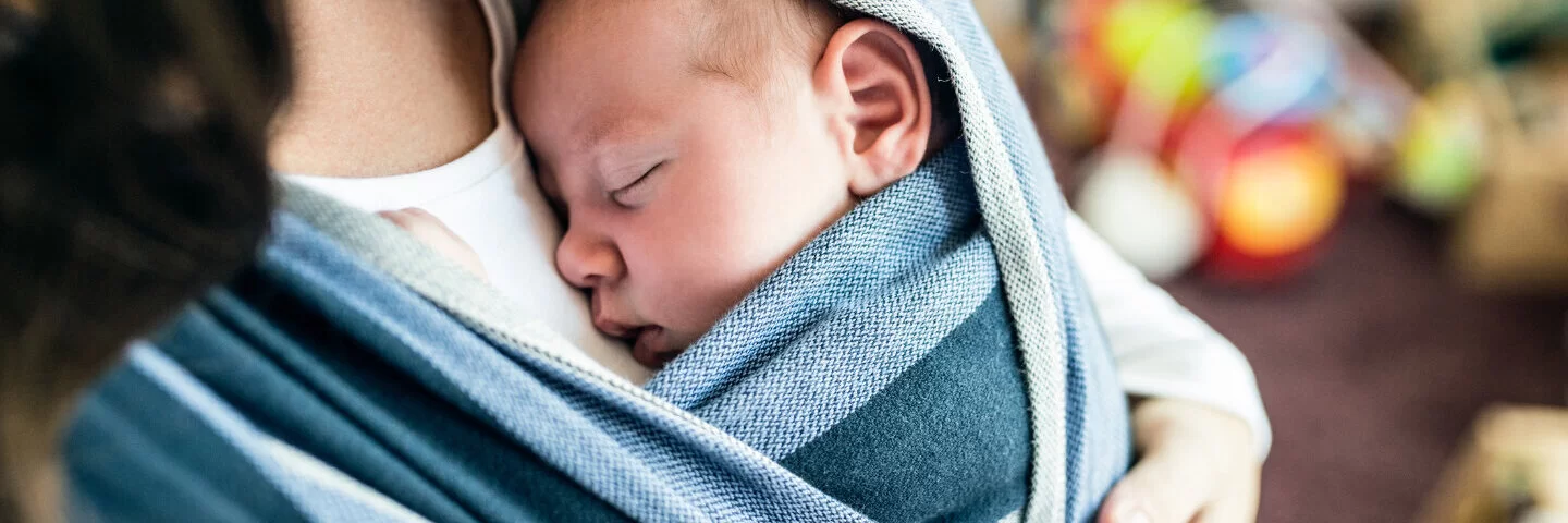 Mutter trägt ihr Baby in einem Tuch vor der Brust.