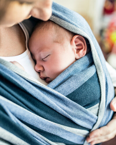 Mutter trägt ihr Baby in einem Tuch vor der Brust.