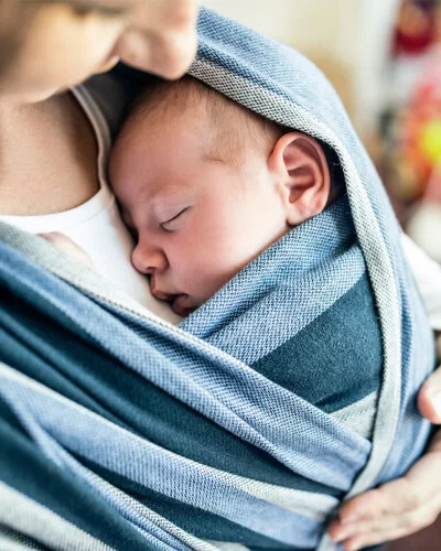 Mutter trägt ihr Baby in einem Tuch vor der Brust.