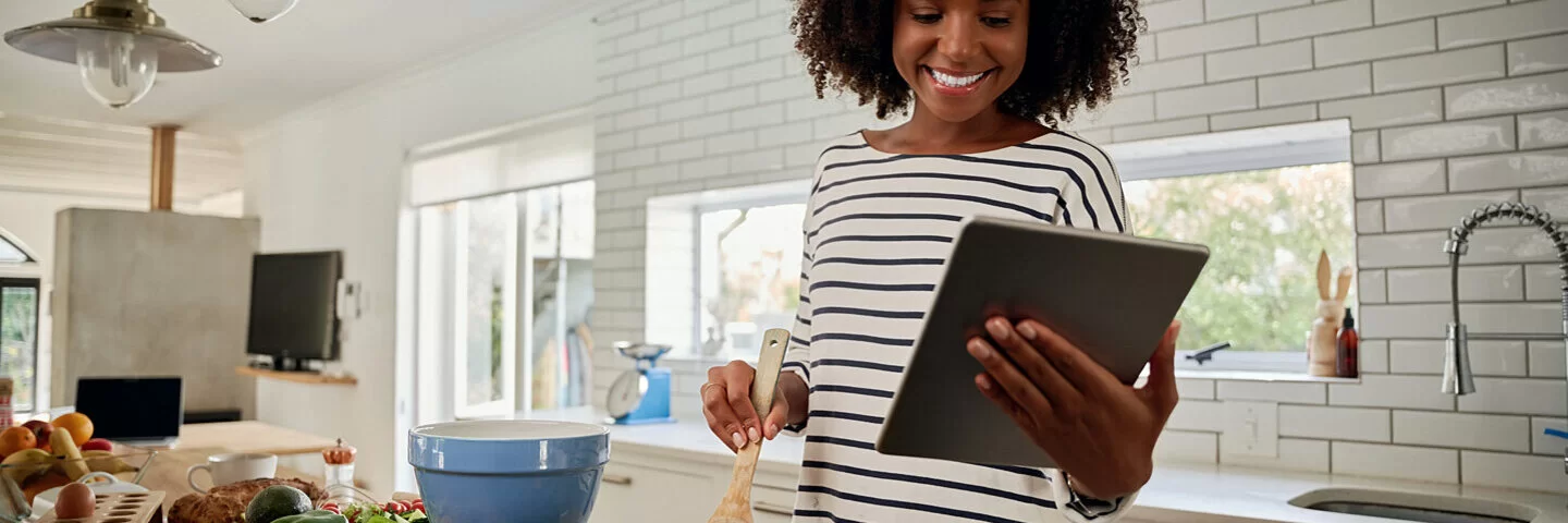 Eine Frau kocht nach einem glutenfreien Rezept, das sie sich auf ihrem Tablet durchliest.