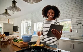 Eine Frau kocht nach einem glutenfreien Rezept, das sie sich auf ihrem Tablet durchliest.