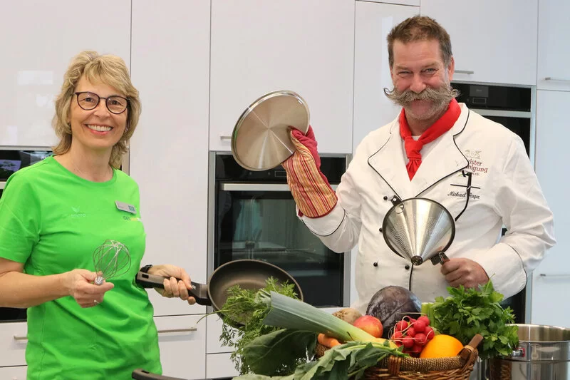 Die Moderatoren der AOK-Kochshow in Heilbronn stehen in der Küche und lächeln in die Kamera.