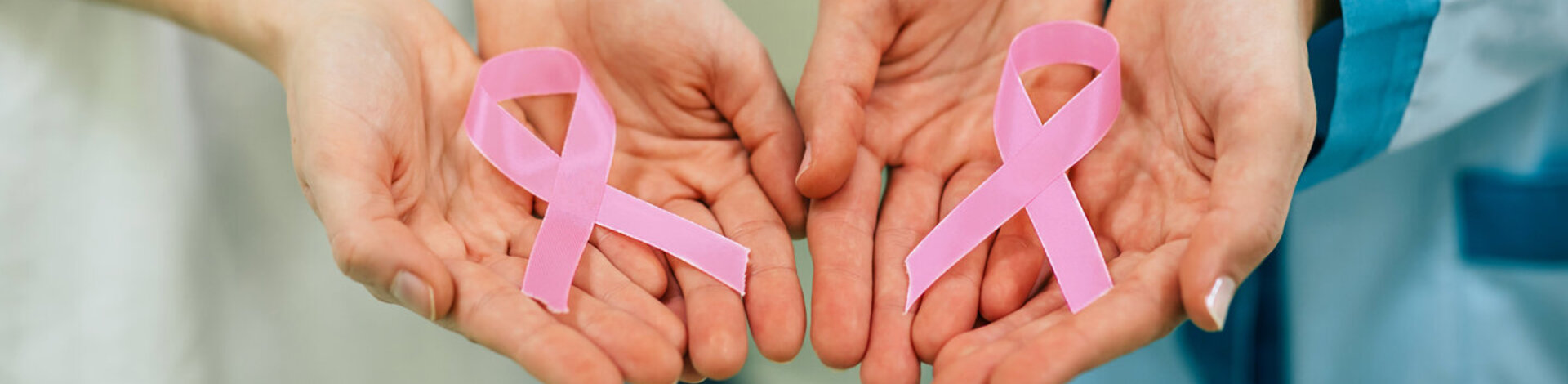 Zwei Frauen halten eine rosa Schleife in der Hand. Das Symbol steht für die Solidarität mit Frauen, die an Brustkrebs erkrankt sind oder ein höheres Brustkrebsrisiko haben.