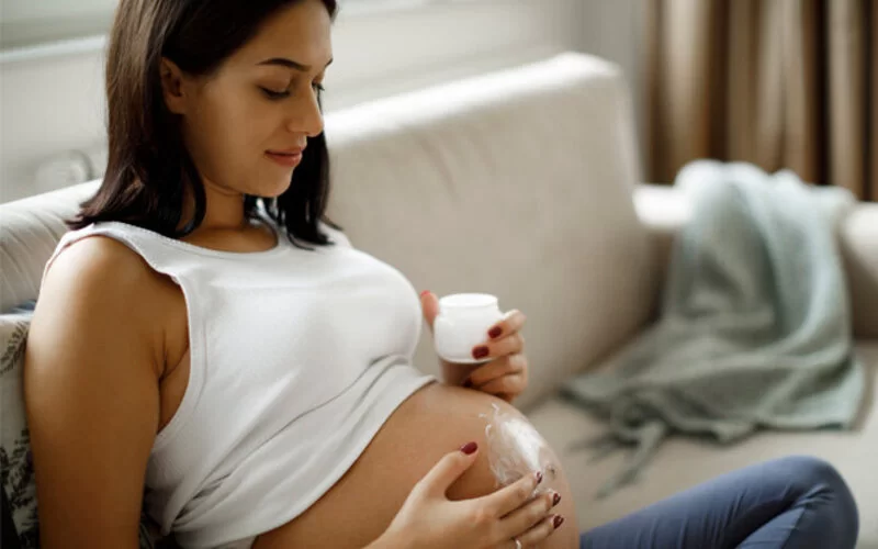 Eine schwangere Frau cremt sich im Sitzen ihren Bauch ein.