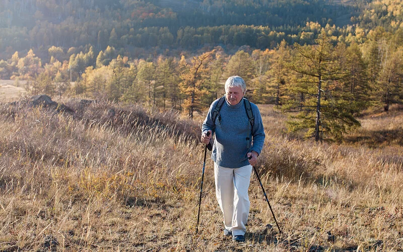 Ein Mann geht in einer Feldlandschaft walken und beugt damit Vorhofflimmern vor.