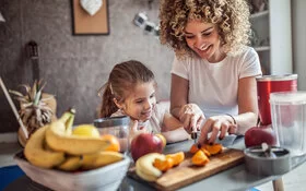 Junge Frau und junges Mädchen schneiden zusammen Obst in kleine Stücke.