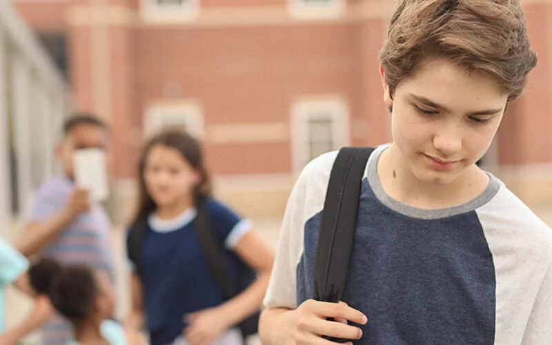 Ein verunsicherter Teenager-Junge mit sozialer Phobie isoliert sich auf dem Schulhof von seinen Mitschülern.