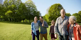 Eine Gruppe von Personen unterschiedlicher Generationen geht über eine Parkwiese und lächelt zuversichtlich in die Kamera. Der Wechsel der Krankenkasse ist leichter, als man denkt.