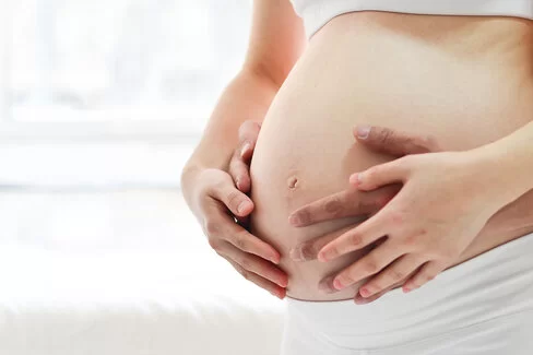 Vier Hände halten zusammen einen Babybauch.