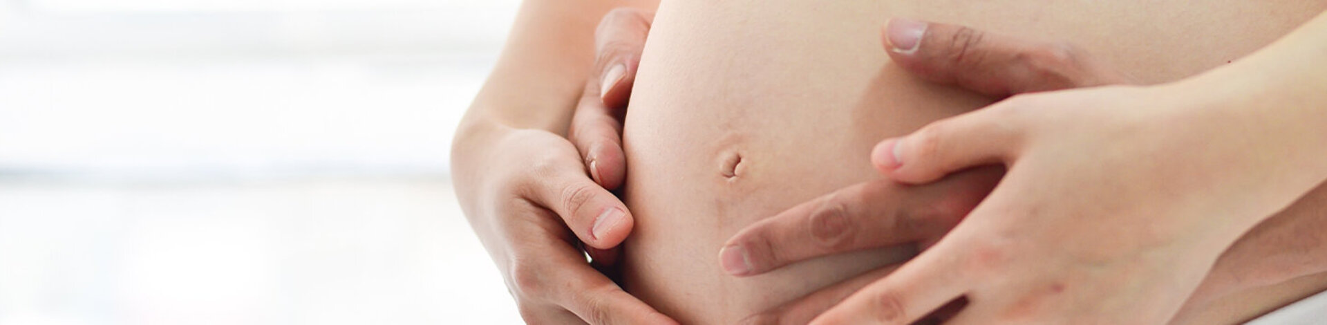 Vier Hände halten zusammen einen Babybauch.