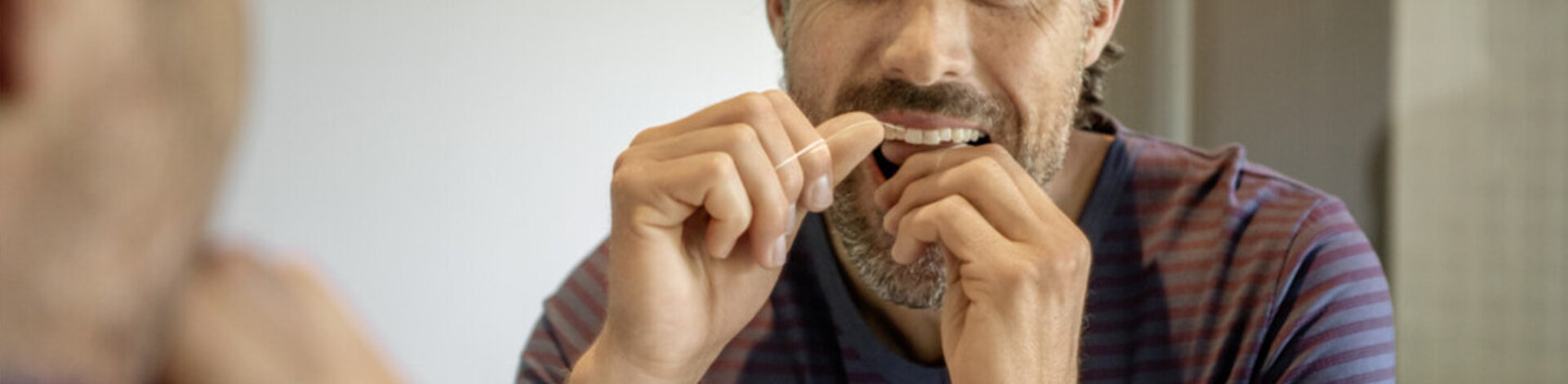 Ein Mann steht vor dem Spiegel und behandelt seine Zähne mit Zahnseide. Die AOK-Zahnklinik ist eine Prophylaxepraxis.