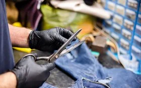 Nahaufnahme von Händen, die mit einer Schere ein Stück Jeans schneiden.