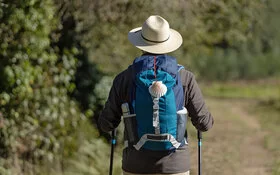 Rückansicht eines Pilgers mit Jakobsmuschel am Rucksack, der einen Feldweg nach Santiago de Compostela nimmt.