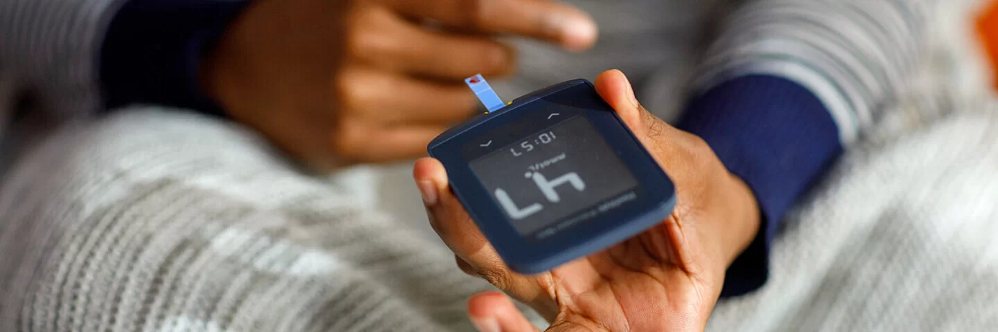 Ein Blutzuckermessgerät, mit dem eine Person im Hintergrund ihren Blutzuckerspiegel untersucht.