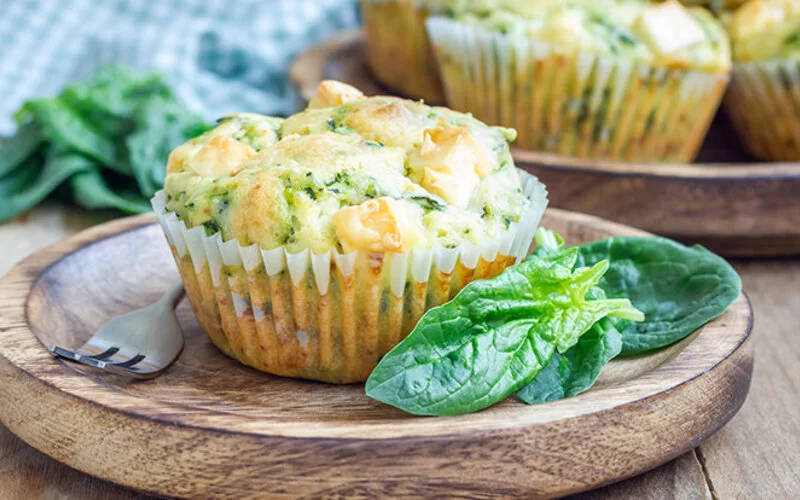 Herzhafte Muffins mit Spinat und Feta auf einem Holzteller serviert