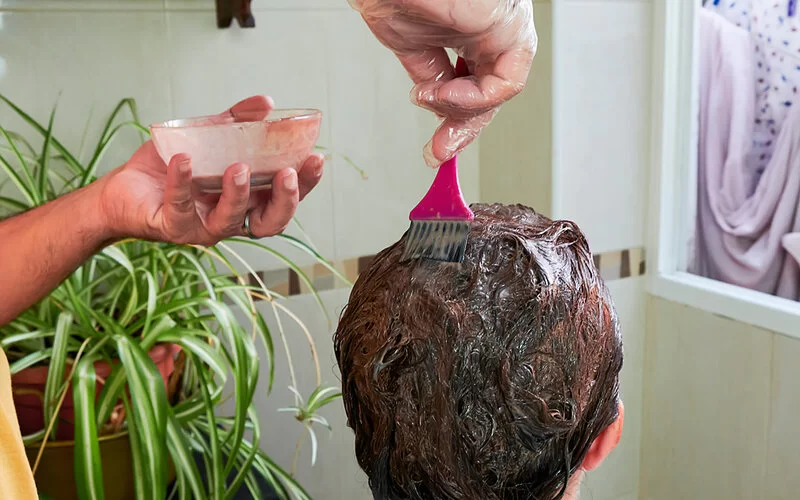 Eine Person färbt einer Frau im Bad die Haare mit einer Naturhaarfarbe.