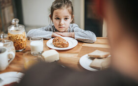 Ein Kind sitzt am Frühstückstisch und möchte das Brötchen vor sich nicht essen.