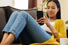 Eine junge Frau sitzt auf einem Sofa und schaut auf ihr Smartphone.