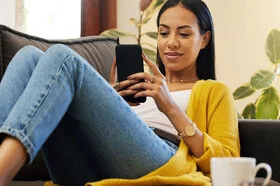 Eine junge Frau sitzt auf einem Sofa und schaut auf ihr Smartphone.
