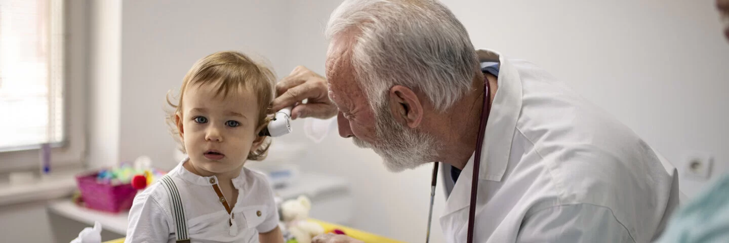 Ein Arzt untersucht ein Kleinkind. Der Arzt schaut sich das Ohr des Kindes von innen an.