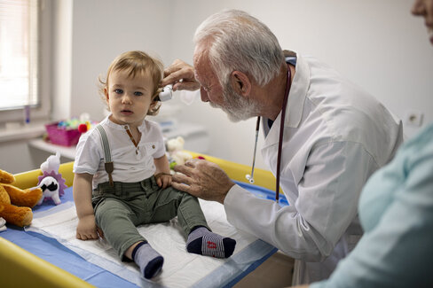 Ein Arzt untersucht ein Kleinkind. Der Arzt schaut sich das Ohr des Kindes von innen an.