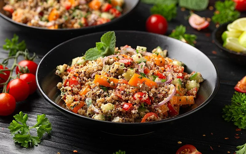Ein Teller enthält Quinoa und verschiedene zubereitete Gemüsesorten: Möhren, Tomaten, Gurke und Zwiebeln.