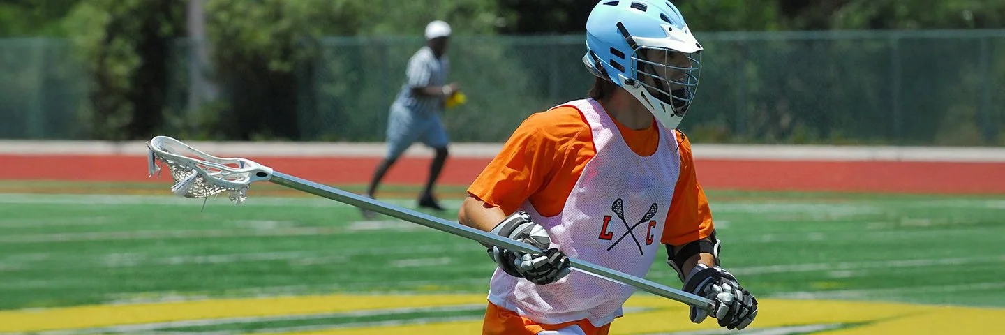 Lacrosse-Spieler mit Schutzausrüstung und Lacrosse-Schläger auf dem Spielfeld.
