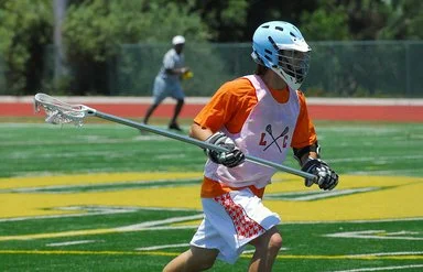 Lacrosse-Spieler mit Schutzausrüstung und Lacrosse-Schläger auf dem Spielfeld.