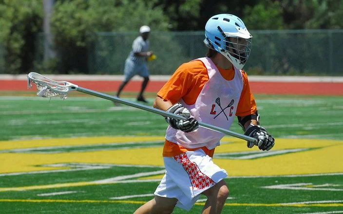 Lacrosse-Spieler mit Schutzausrüstung und Lacrosse-Schläger auf dem Spielfeld.