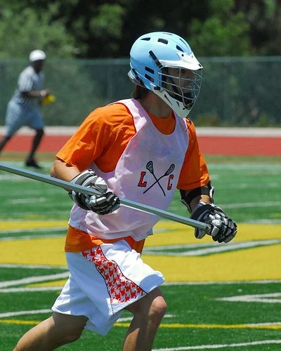 Lacrosse-Spieler mit Schutzausrüstung und Lacrosse-Schläger auf dem Spielfeld.
