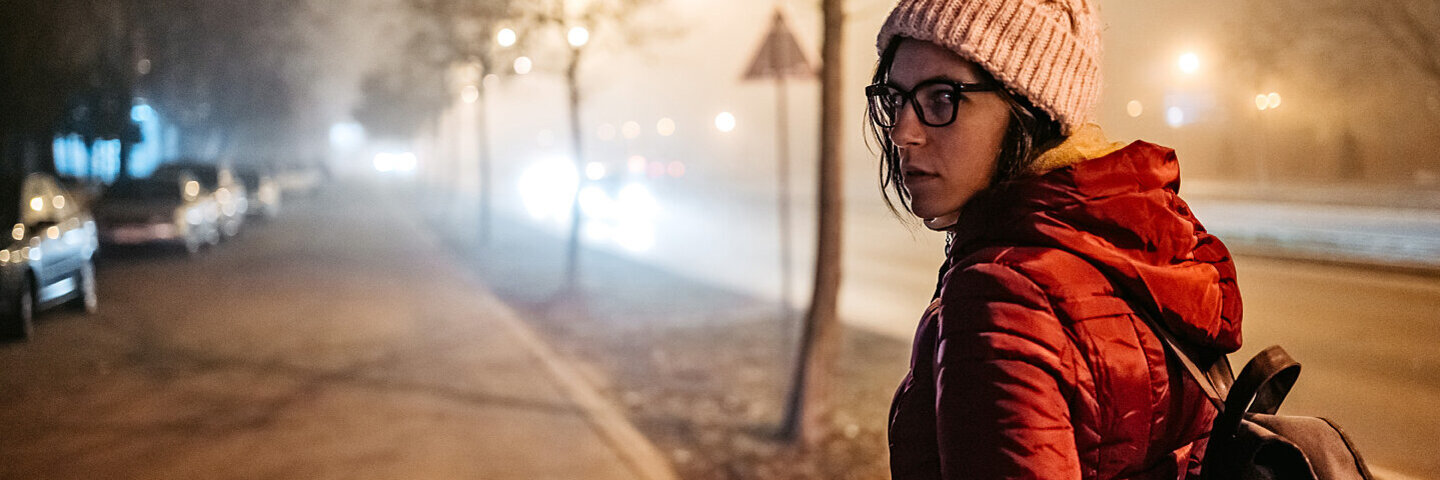 Eine Frau blickt sich ängstlich schauend um, während sie in der Dunkelheit allein eine Straße entlang geht.