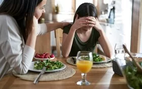 Frau sitzt am Esstisch und unterstützt ihre Tochter beim Thema Essstörungen
