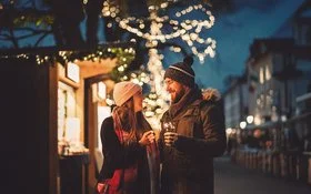 Paar mit Mützen hält Wunderkerzen auf einem abendlichen, festlich beleuchteten Weihnachtsmarkt in Hessen.