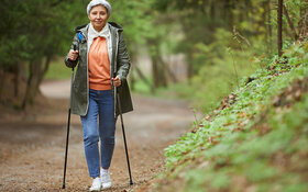 Ältere Frau beim Walken im Wald und das trotz einer Kniearthrose.