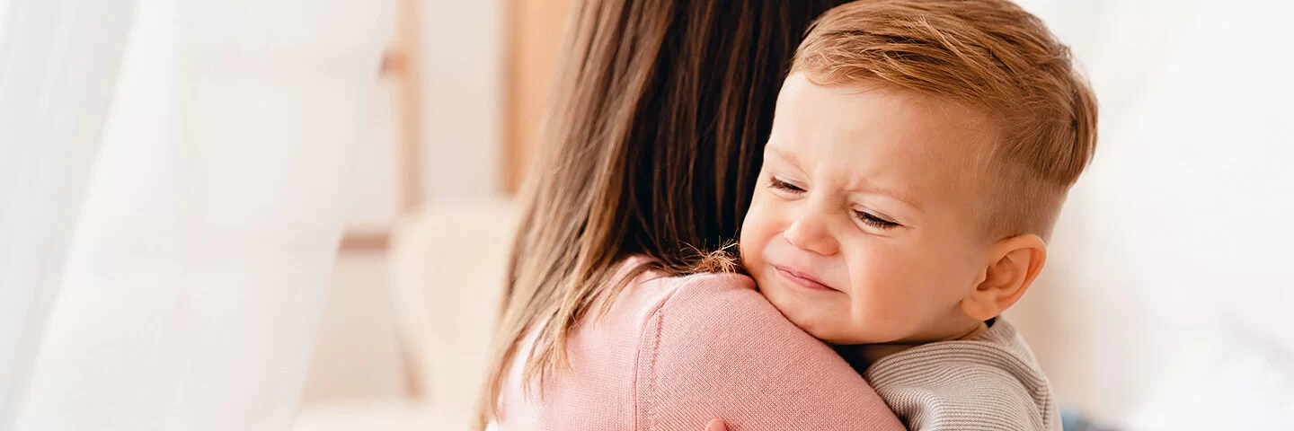 Eine Frau hält ein Kind auf dem Arm, dessen Blick Schmerzen vermuten lässt.