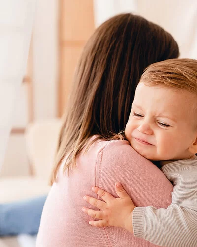 Eine Frau hält ein Kind auf dem Arm, dessen Blick Schmerzen vermuten lässt.