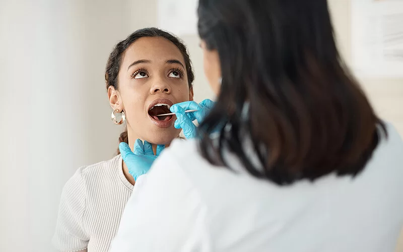 Eine Ärztin nimmt mit einem Teststäbchen einen Abstrich von der Mundschleimhaut bei einer jungen Patientin, um sie auf Mundsoor zu testen.