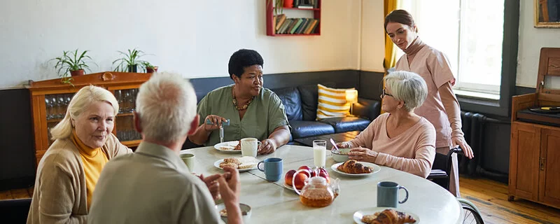 Eine Gruppe älterer Menschen werden von Pflegerin umsorgt.