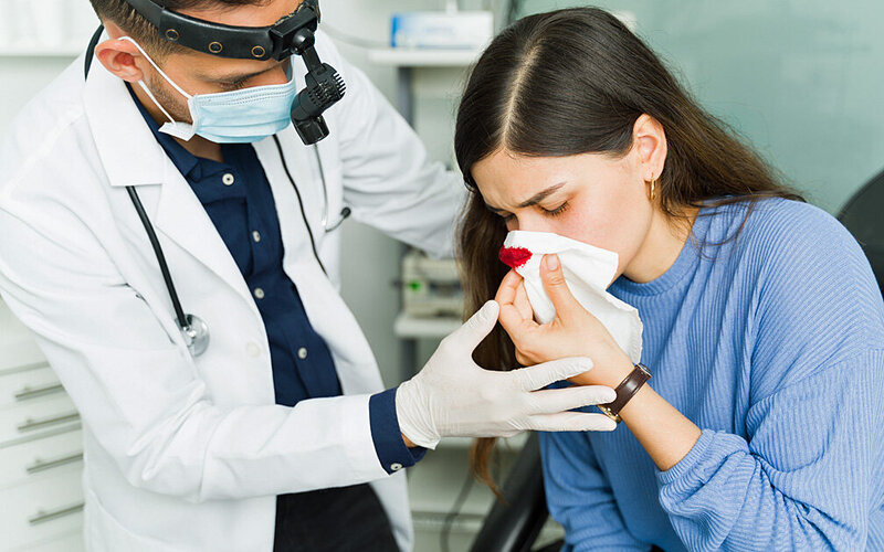 Eine Frau ist mit Nasenbluten bei einem Arzt.