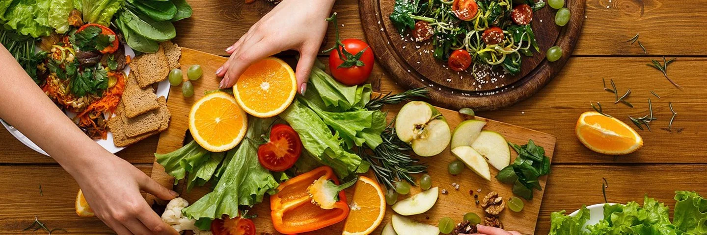 Mehrere Hände greifen nach geschnittenem Obst und Gemüse auf Schneidebrettern.