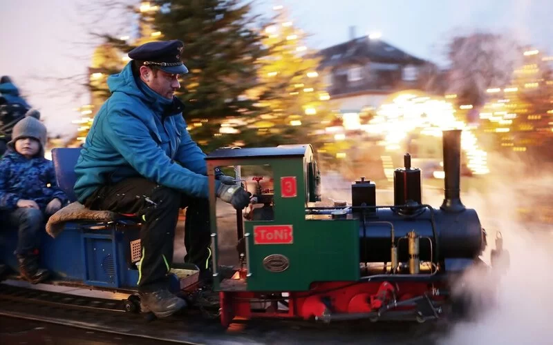 Ein Schausteller fährt eine kleine Eisenbahn für Kinder auf einem Weihnachtsmarkt.